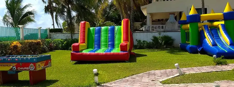 Dos brincolines inflables y una mesa de futbolito en un jardín.